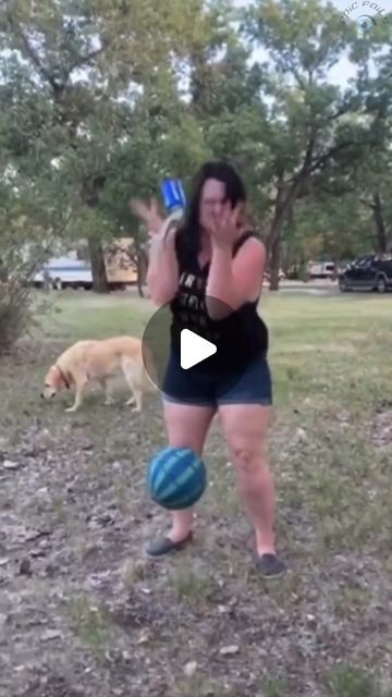 a woman is playing with a ball and a dog in the park while talking on her cell phone