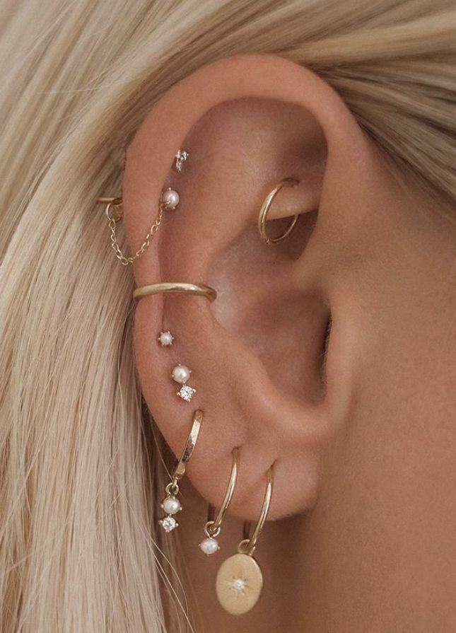 a woman with blonde hair wearing gold ear cuffs and pearled earrings on her left ear