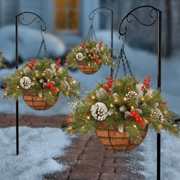 two hanging baskets filled with pine cones and red berries on top of snow covered ground