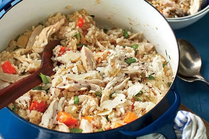 a blue pot filled with chicken and rice on top of a table next to two silver spoons