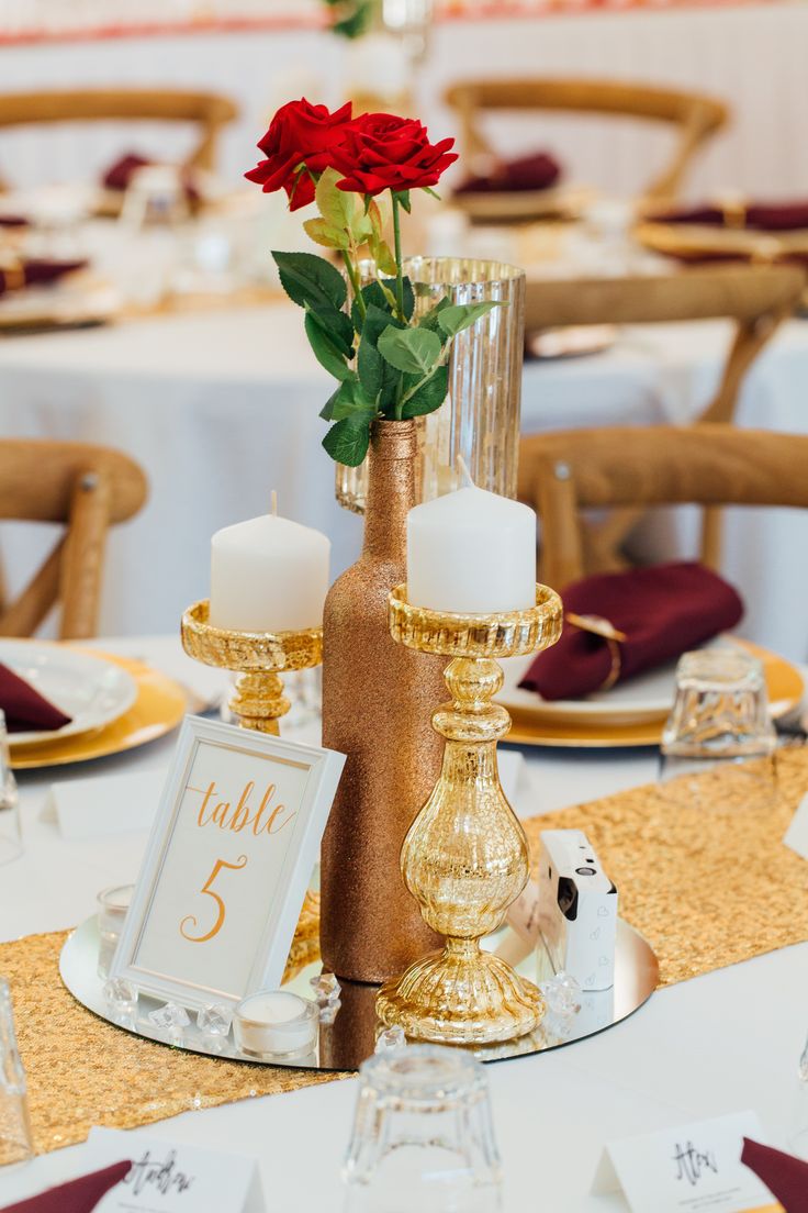 the table is set with gold and white plates, candles, and flowers in vases