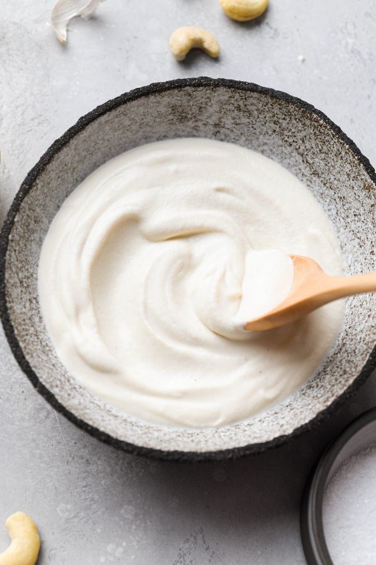 a wooden spoon in a bowl filled with yogurt next to cashews