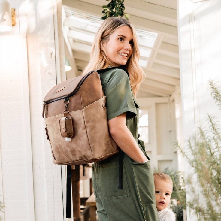 a woman carrying a large brown bag while standing next to a baby