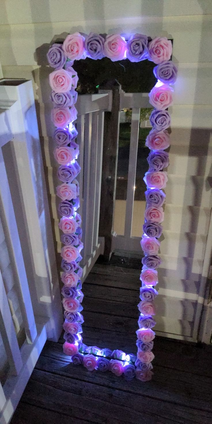 a mirror that has flowers on it and some lights in the frame around it, sitting on a wooden floor