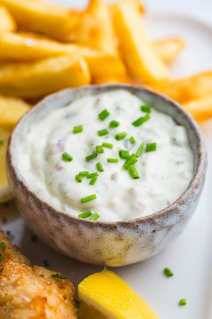 a white plate topped with fish and fries next to a bowl of ranch dressing on top of it