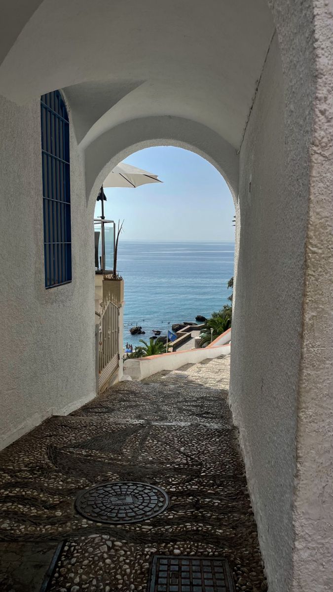 an archway leading to the ocean with blue shutters on either side and a white umbrella over it