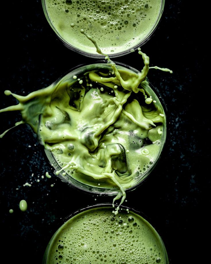 two glasses filled with green liquid on top of a black table next to each other