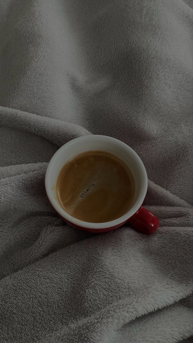 a cup of coffee sitting on top of a bed covered in gray sheets and blankets