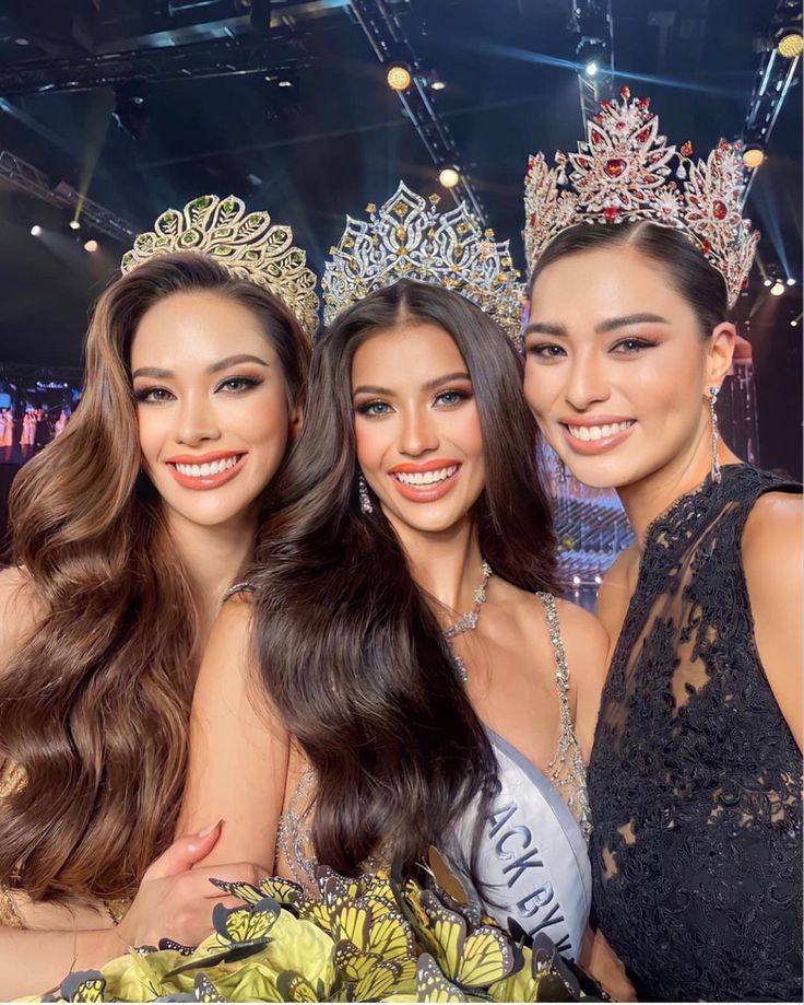 three beautiful women standing next to each other in front of a stage wearing tiaras