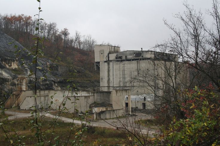 an abandoned factory sits on the side of a hill with trees in front of it