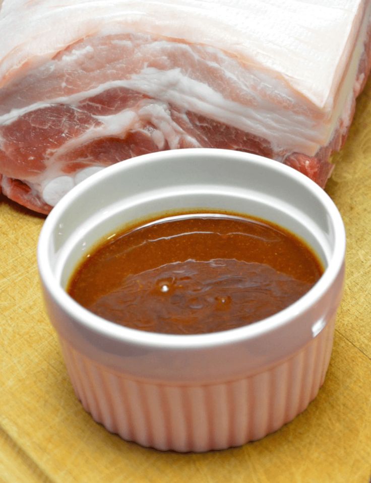 a small white bowl filled with sauce next to a piece of meat