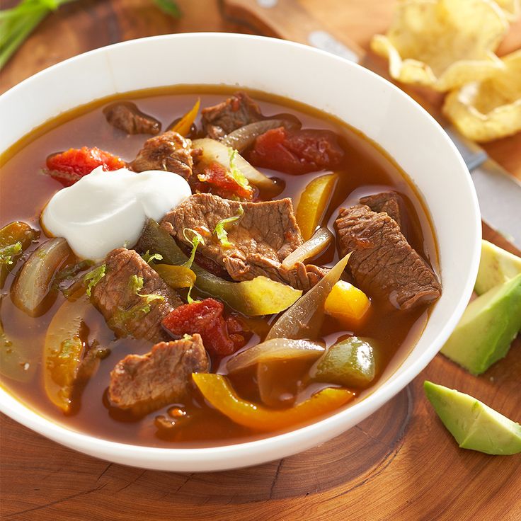 a bowl of beef and vegetable soup with sour cream on the top is ready to be eaten