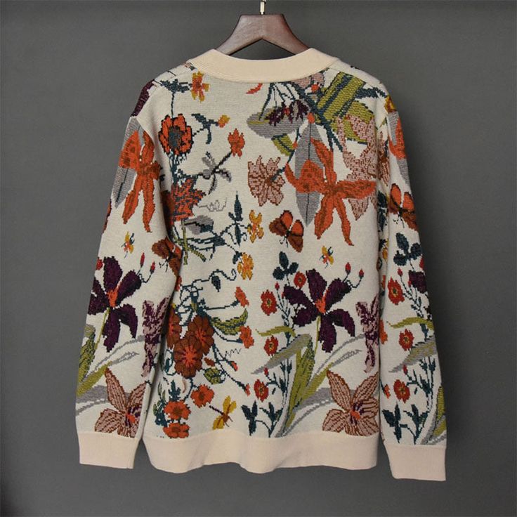 a white sweater with colorful flowers on it hanging from a hanger against a gray wall