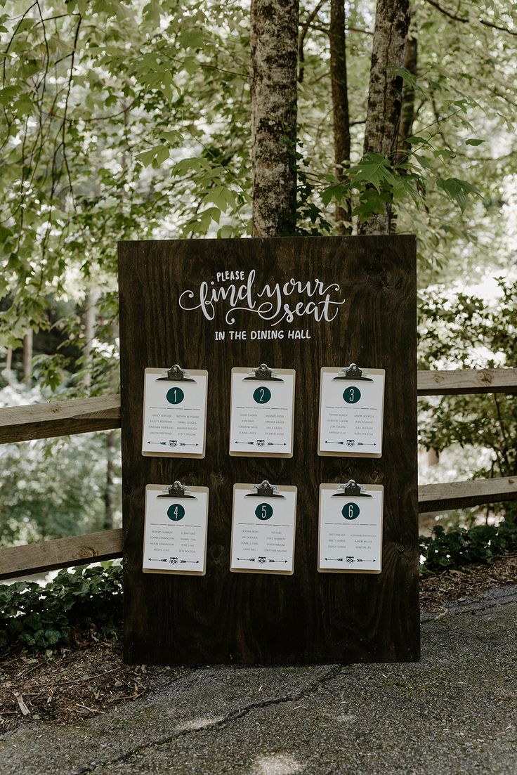 a wooden sign sitting on the side of a road next to a lush green forest