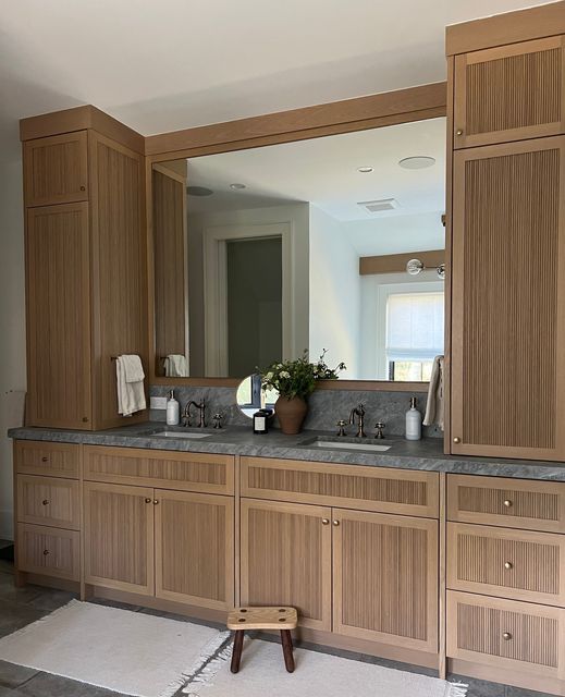 a large bathroom with wooden cabinets and gray counter tops, along with a stool in front of the mirror