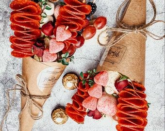 two cones filled with strawberries and other fruit on top of paper wrapped in twine