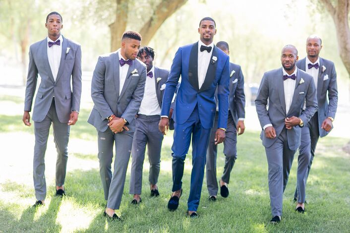 a group of men in suits and bow ties walking through the grass with trees behind them