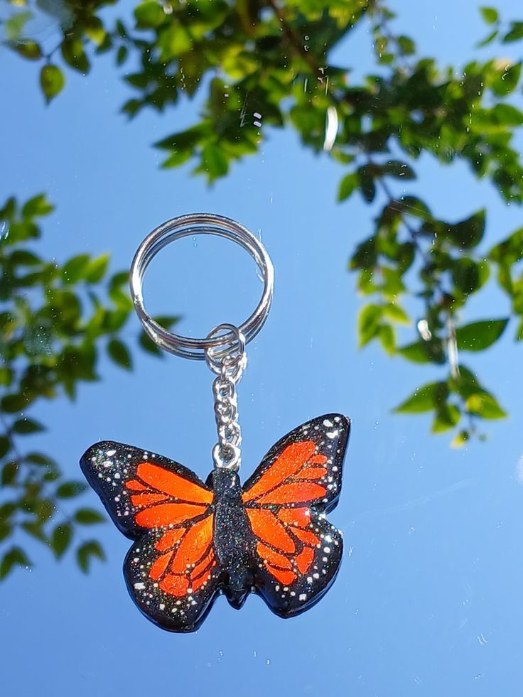 an orange butterfly keychain hanging from a tree branch with leaves in the background