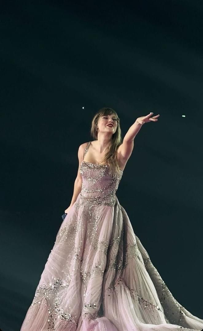 a woman in a pink dress standing on top of a stage with her arms out