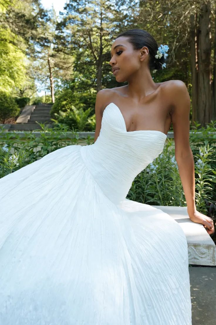 a woman in a white wedding dress sitting on a bench with her hand on her hip