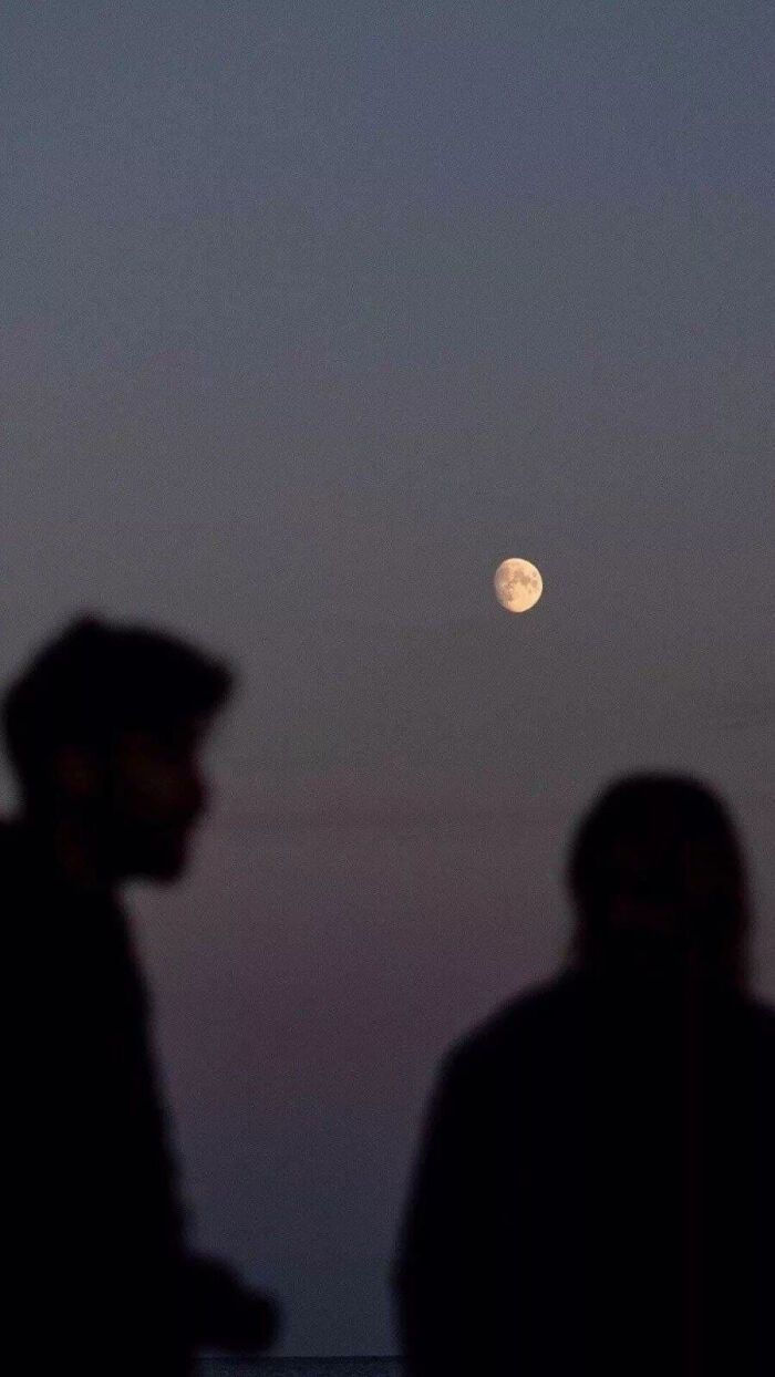 two people are standing in front of the moon