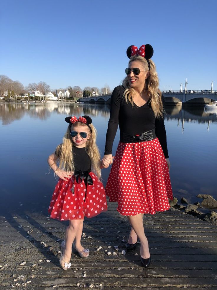 two women in minnie mouse costumes standing on a dock next to a body of water