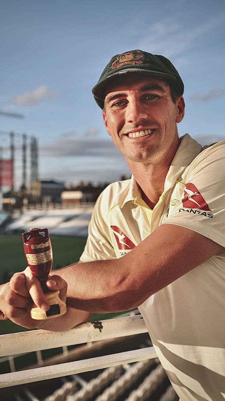 a man holding a glass of beer on top of a wooden fence next to a field