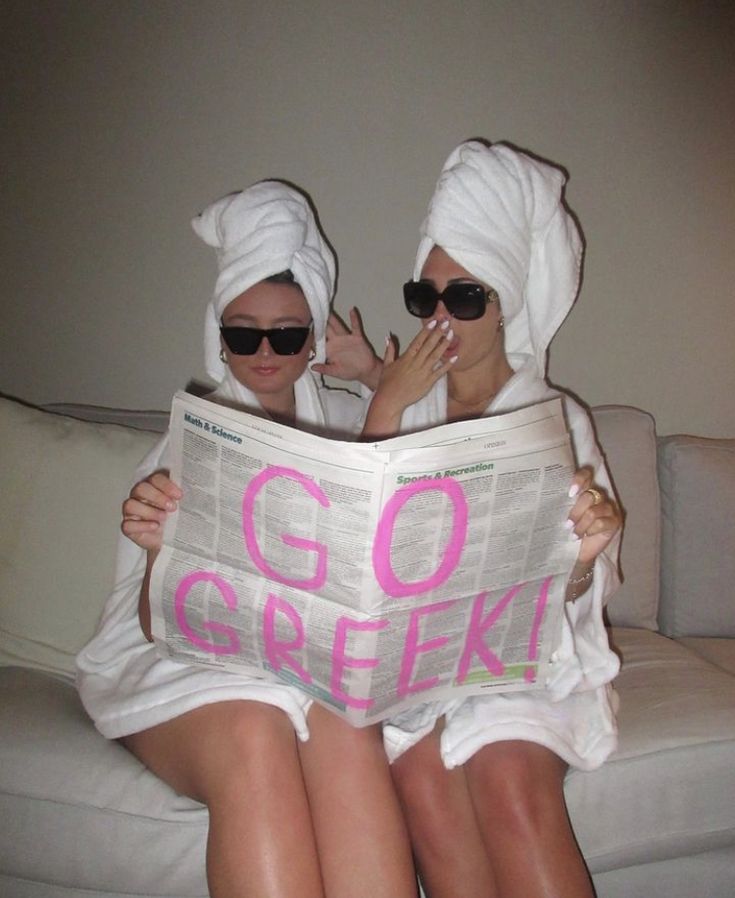 two women sitting on a couch with towels wrapped around their heads and reading a newspaper