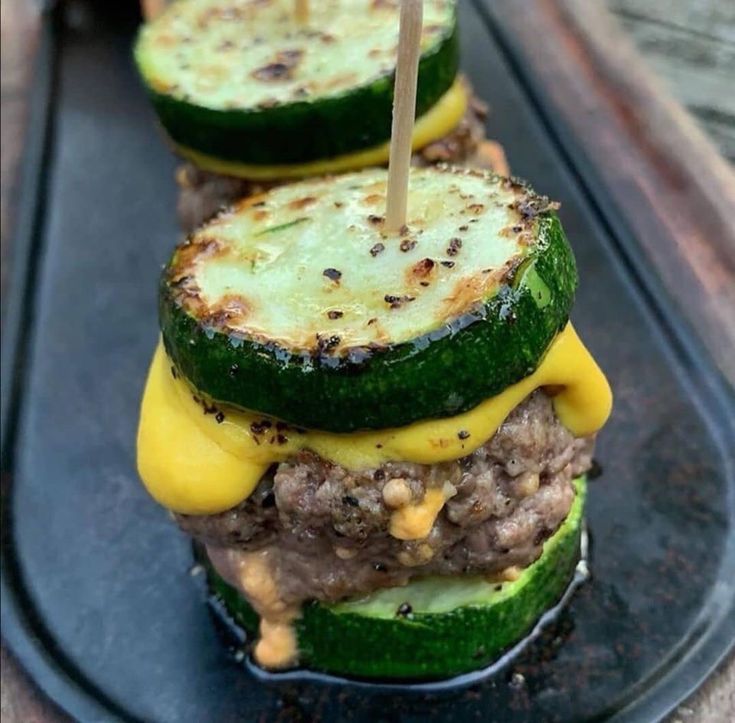 two cucumber sandwiches on a black plate with toothpicks sticking out of them