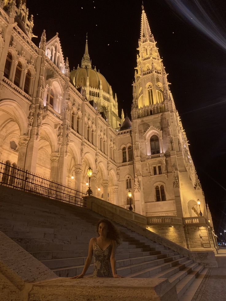 a woman is sitting on some steps in front of a building at night with lights