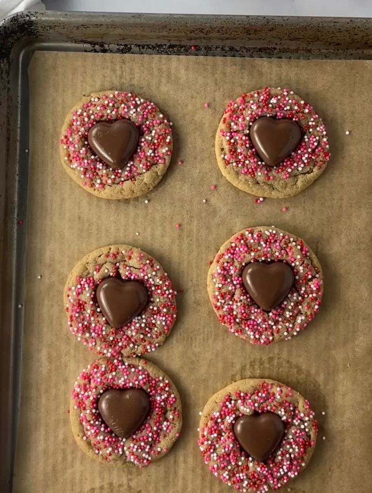 six heart shaped cookies with sprinkles on a baking sheet, ready to be baked