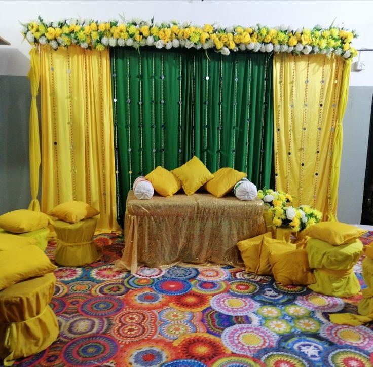 a decorated stage with yellow drapes, pillows and flowers on the table in front of it