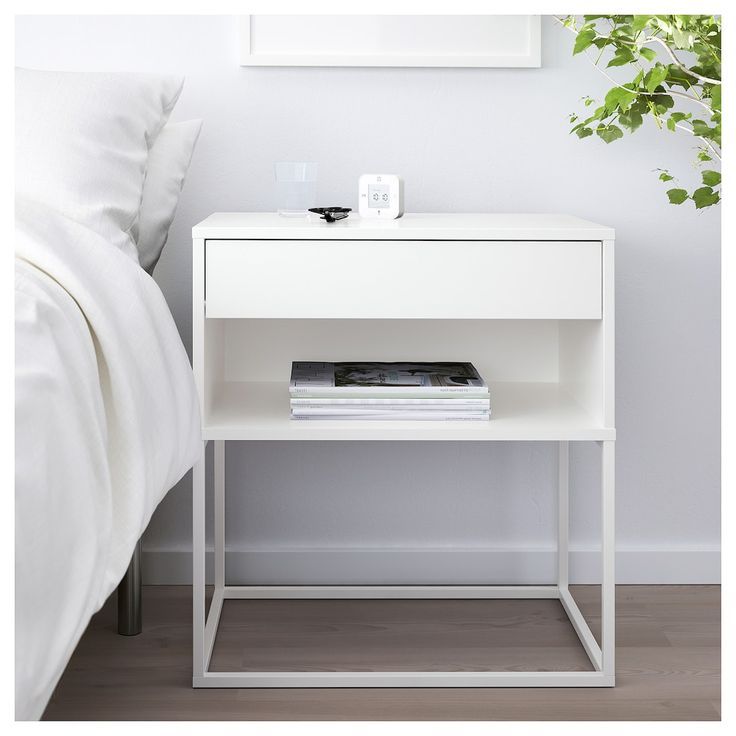 a white nightstand next to a bed with a plant on it and a painting hanging above