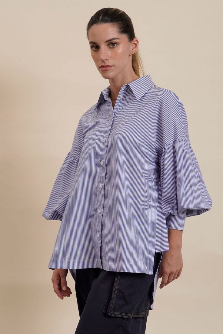 This elegant Cotton Blouse combines timeless style with comfort. Crafted from Pima Cotton, it features a classic striped pattern in muted colors. The relaxed fit ensures breathability, while the distinctive ruffle detailing on the sleeves adds a contemporary touch. Complete with a sharp collar and button-down front, this top is perfect for both casual and semi-formal occasions.- Breathable and comfortable fabric.- Classic Striped Pattern.- Oversized for easy styling.- Button-down front and sharp Spring Cotton Blouse With Striped Sleeves, Striped Shirt For Office In Spring, Elegant Striped Relaxed Fit Tops, Chic Vertical Stripes Blouse For Spring, Chic Spring Blouse With Vertical Stripes, Spring Office Blouse With Vertical Stripes, Spring Blouse With Vertical Stripes And Relaxed Fit, Elegant Tops With Vertical Stripes For Spring, Chic Pinstripe Tops For Office