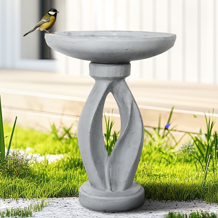 a bird is perched on the edge of a fountain in the grass near some flowers