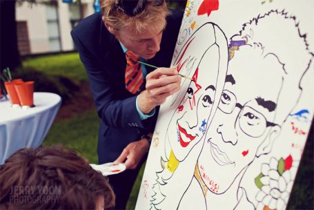 a woman is drawing on a canvas while another man watches from the sidelines at an outdoor event