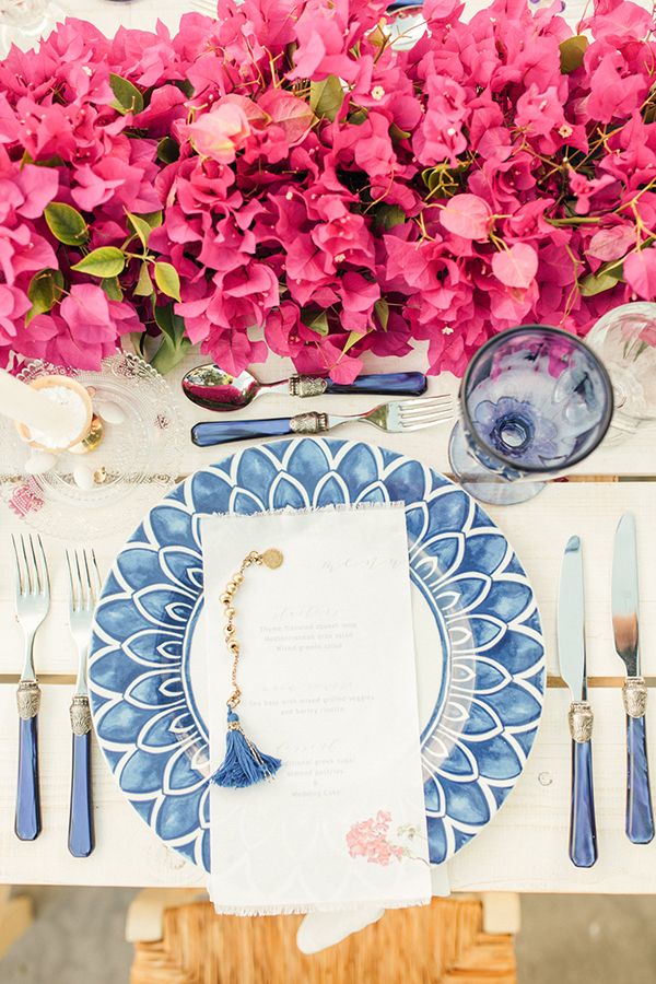 the table is set with blue and white plates, silverware, and pink flowers