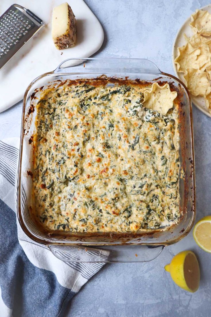 a casserole dish with spinach, cheese and tortilla chips on the side