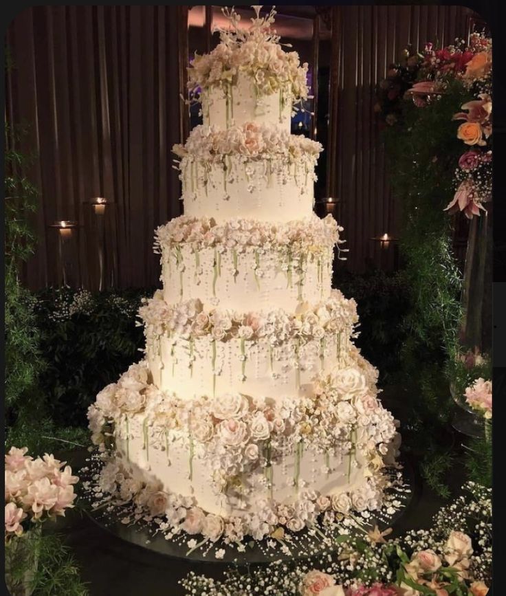 a large white wedding cake sitting on top of a table covered in flowers and greenery