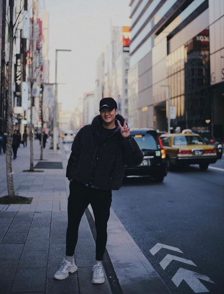 a man is standing on the side walk talking on his cell phone while wearing a hat