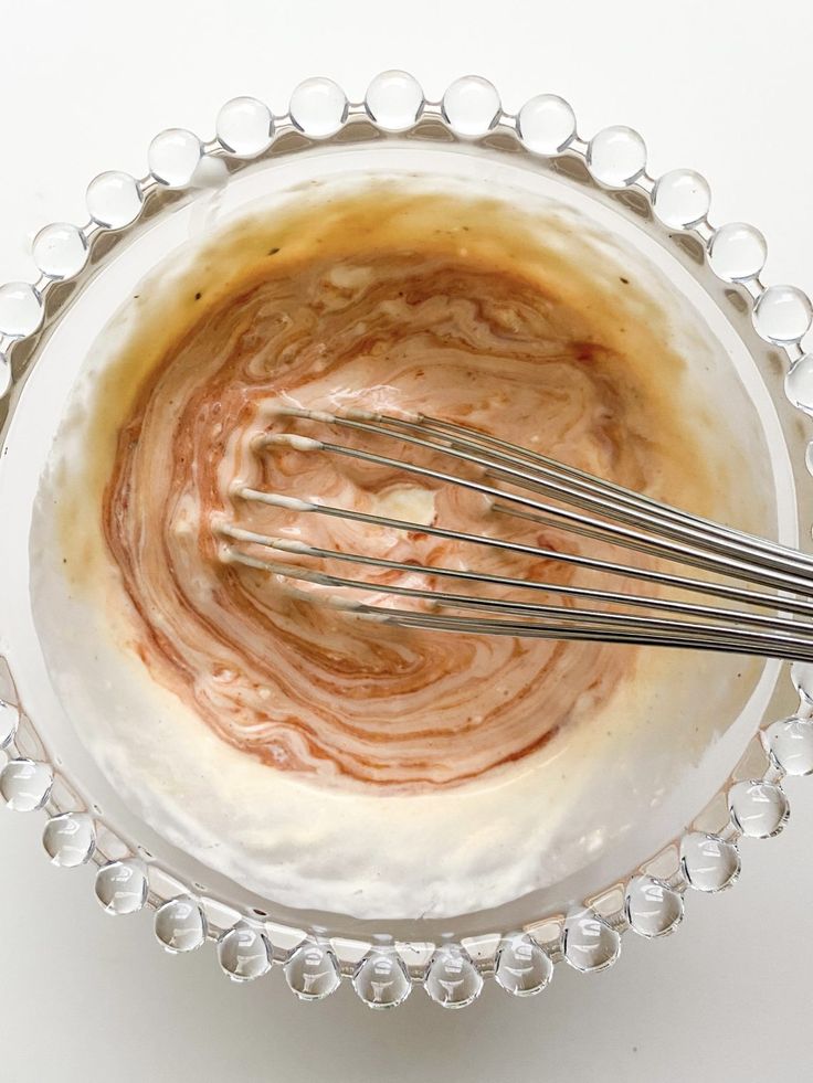 a glass bowl filled with liquid and whisk