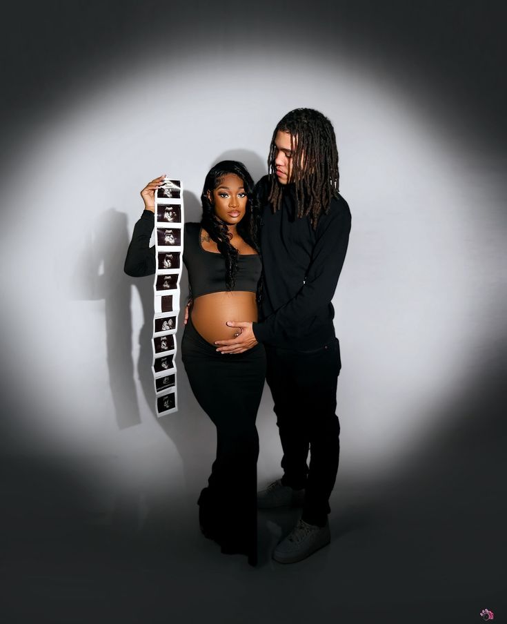 a pregnant woman standing next to a man with dreadlocks on his head and holding a sign