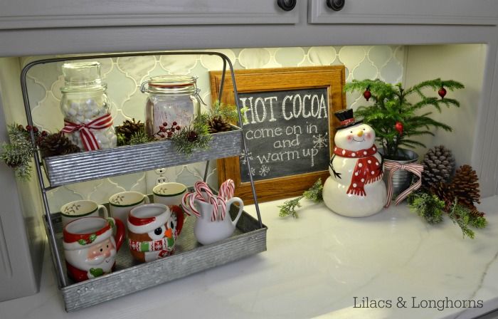 a kitchen counter with christmas decorations and coffee mugs on the shelf above it is a sign that says hot cocoa