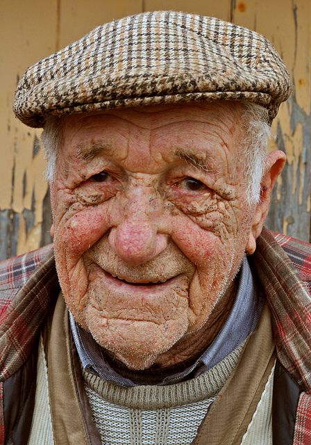 an old man with wrinkles and a hat on his head is looking at the camera