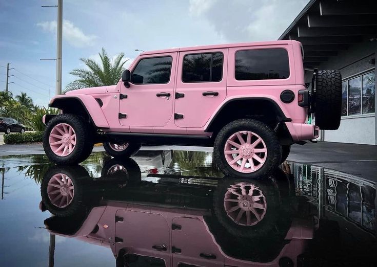 a pink jeep is parked in front of a building with its reflection on the water