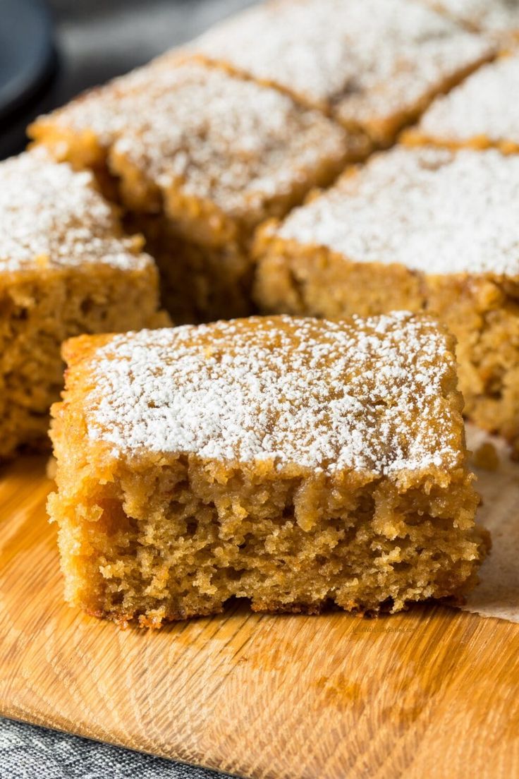 a wooden cutting board topped with slices of cake covered in powdered sugar and sitting on top of a table