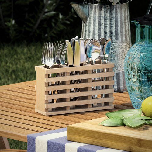 a wooden crate with forks and knives in it on a table next to a blue vase