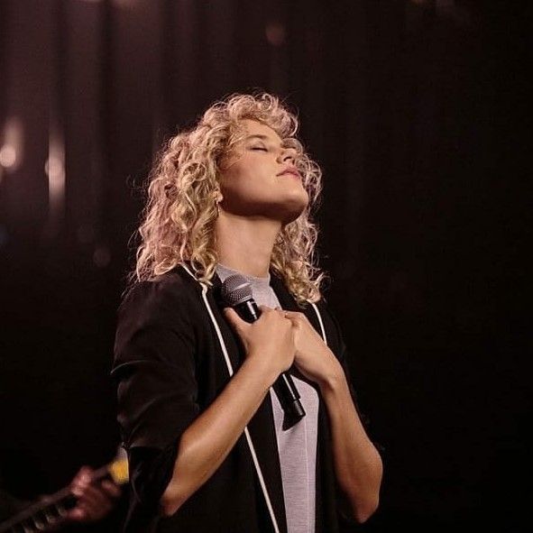 a woman singing into a microphone while standing in front of a stage with lights behind her