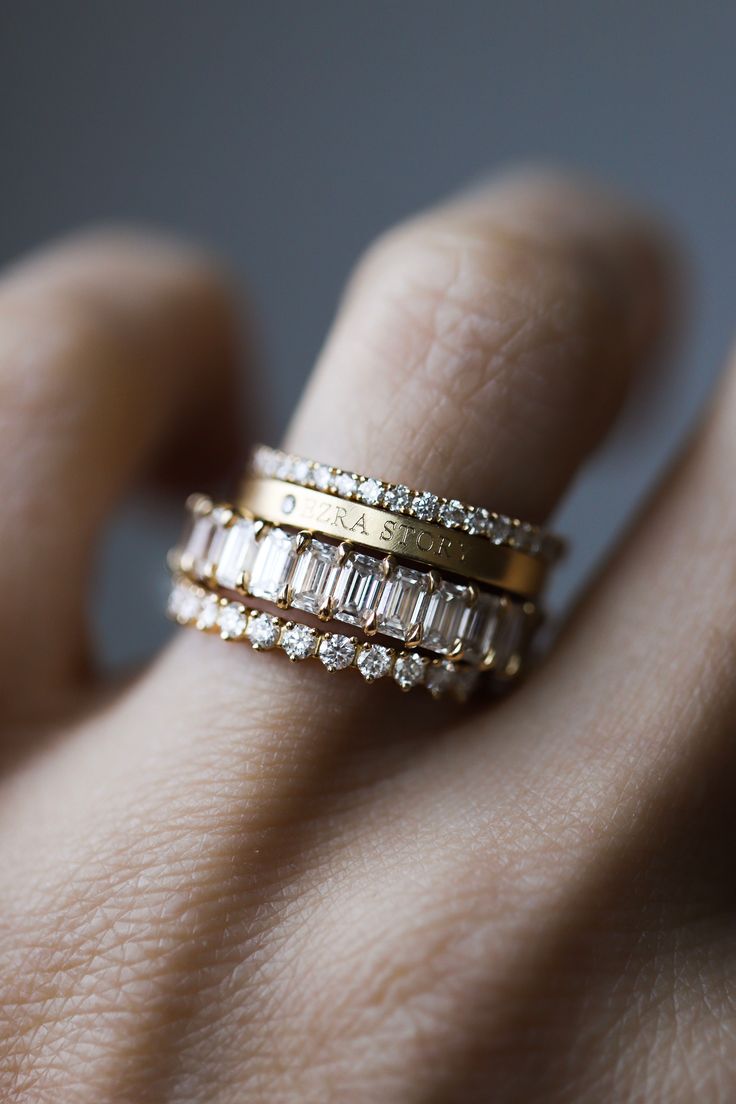 a woman's hand with three gold rings on top of her finger and two diamonds in the middle