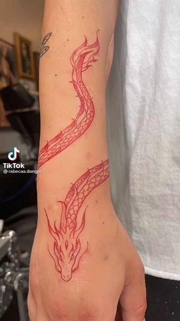 a hand with a red dragon tattoo on it's left arm and the wrist